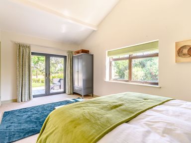 A bedroom with a bed green throw a blue rug gray wardrobe glass doors and a window at The Paddock in Honington near Shipston-On-Stour