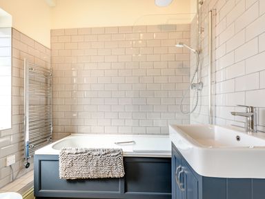 A bathroom with a bathtub shower combination a sink with cabinet and a towel on the bathtub at The Paddock in Honington near Shipston-On-Stour