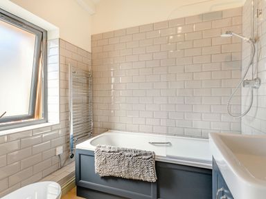 A bathroom with a bathtub a shower a towel rail a window and a sink at The Paddock in Honington near Shipston-On-Stour