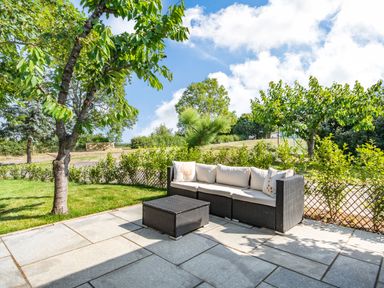 An outdoor patio with a black wicker sofa and table surrounded by trees and greenery at The Paddock in Honington near Shipston-On-Stour