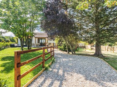 An outdoor area with a gravel driveway lined by a wooden fence leading to a house with patio furniture at The Paddock in Honington near Shipston-On-Stour