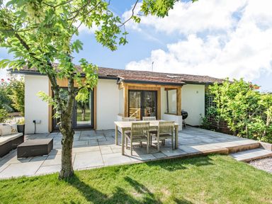 An outdoor patio area with wooden table and chairs a tree and a white house at The Paddock in Honington near Shipston-On-Stour