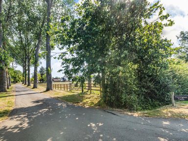 A paved road lined with trees next to a fenced field and a sign reading Honington Fields at The Paddock in Honington near Shipston-On-Stour