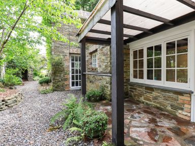 A stone patio with potted plants and a covered porch next to a gravel path and stone building at The Cottage in St Kew