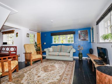 A living room with a striped sofa and armchairs a wooden bench a TV on a wooden stand and plants at The Cottage in St Kew