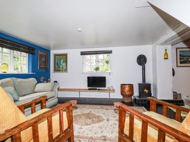 A living room with wooden armchairs a striped sofa a wood stove and a tv on a wooden stand at The Cottage in St Kew