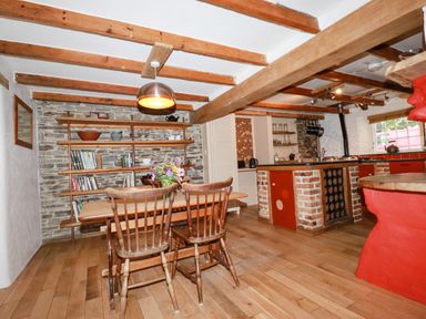 A kitchen and dining area with wooden beams wooden chairs wooden table open shelves and a brick island at The Cottage in St Kew