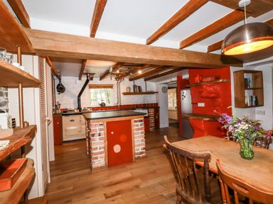 A kitchen with wooden beams exposed on the ceiling a brick island a wooden dining table with chairs and flowers in a vase at The Cottage in St Kew