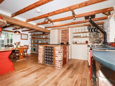 A kitchen with wooden beams a brick island and a dining table with chairs at The Cottage in St Kew