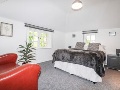 A bedroom with a bed a red armchair a plant and windows at The Cottage in St Kew