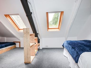 An attic bedroom with two beds a wooden shelf and skylight windows at The Cottage in St Kew