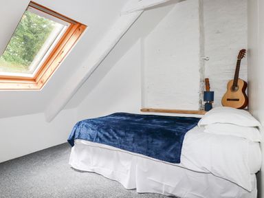 A bedroom with a single bed covered with a blue blanket near a skylight window and a guitar on a shelf at The Cottage in St Kew