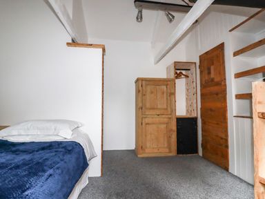 A bedroom with a bed with white pillows and blue blanket and wooden furniture at The Cottage in St Kew