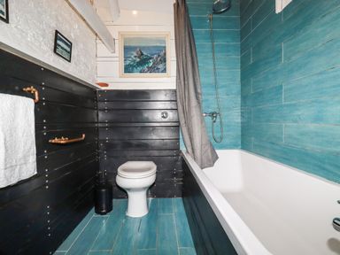 A bathroom with a toilet bathtub shower gray curtain and paintings on the wall at The Cottage in St Kew