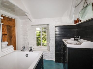 A bathroom with a bathtub towels a window a sink with a mirror and wooden door at The Cottage in St Kew