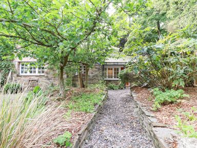 A gravel pathway leading to a stone house surrounded by trees and plants at The Cottage in St Kew