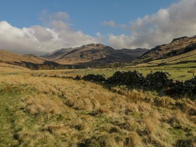 A grassy field with a stone wall and hills in the background at The Residence in Cleator