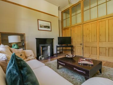 A living room with a sofa cushions a coffee table a television a fireplace and wooden paneling at The Residence in Cleator