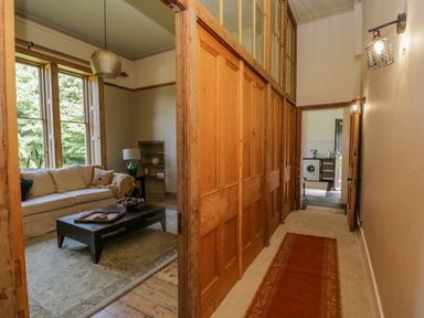 A hallway with wooden sliding doors and carpet runner leading to a living room with sofa and coffee table and a kitchen with washing machine in the background at The Residence in Cleator