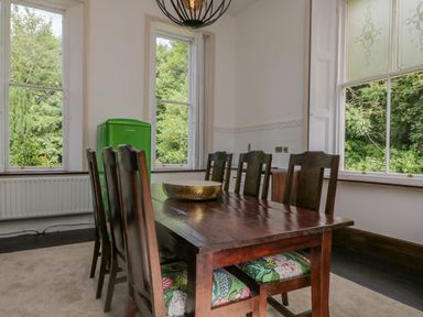 A dining room with a wooden table and six chairs near large windows with a green fridge in the corner at The Residence in Cleator