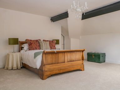 A bedroom with a wooden bed with pillows a lamp on a table and a green trunk at The Residence in Cleator