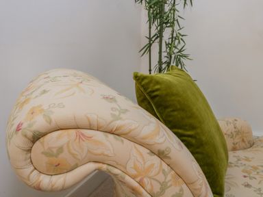 A close up of a floral patterned sofa with a green cushion and a tall plant in the corner at The Residence in Cleator