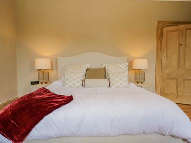 A bed with white bedding and multiple pillows a red blanket on the bed two bedside tables with lamps and an open wooden door at The Residence in Cleator