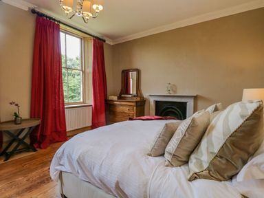 A bedroom with a bed with pillows a wooden dresser a mirror red curtains and a small table with a plant at The Residence in Cleator