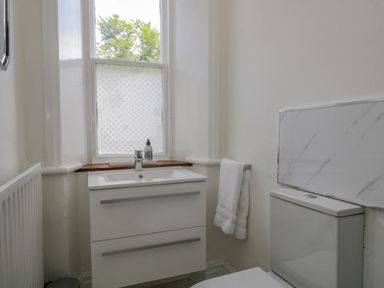 A bathroom with a sink cabinet under a window and a toilet with a marble panel behind it at The Residence in Cleator