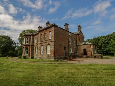 A large two story brick house with chimneys and a patio with table and umbrella on a lawn at The Residence in Cleator