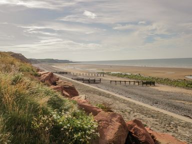 A coastline with a sandy beach green grass rocks and a pathway at The Residence in Cleator