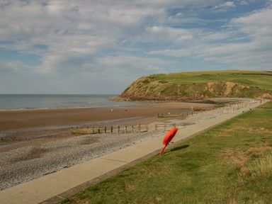 A beach with a concrete pathway green grass and a hill in the background at The Residence in Cleator