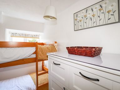 A bedroom with a wooden bunk bed a white dresser with a basket and wall art at Gwynn Cottage in St Mabyn