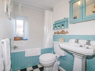 A bathroom with a bathtub shower combination toilet and sink with blue paneling at Gwynn Cottage in St Mabyn