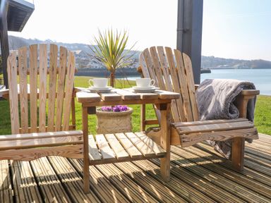 Two wooden chairs with teacups on a wooden table between them on a deck overlooking water at White Sails in Y Felinheli