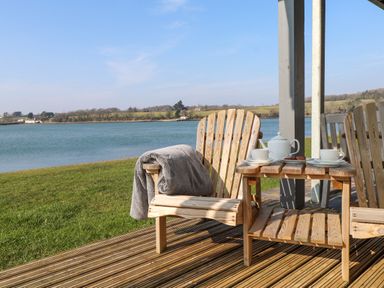 A wooden deck with two wooden chairs and a table holding a teapot and cups by a river at White Sails in Y Felinheli