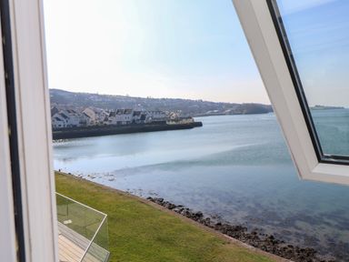 A view of a waterfront with houses along the shore and a grassy area by the water at White Sails in Y Felinheli