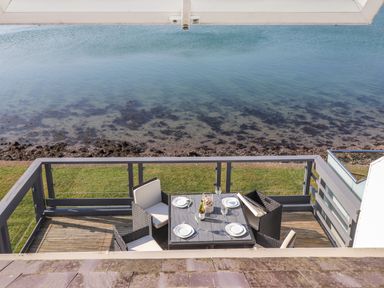 An outdoor dining area with a table and four chairs facing a waterfront at White Sails in Y Felinheli