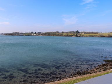 A body of water with a shoreline and buildings in the distance at White Sails in Y Felinheli