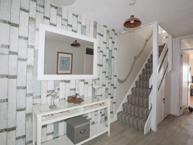 A hallway with striped carpeted stairs a white console table with bird decorations and a large white framed mirror on a wooden plank patterned wall at White Sails in Y Felinheli