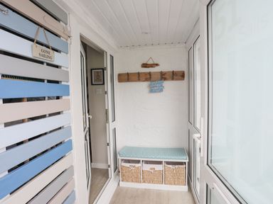 A small enclosed porch with a bench with storage baskets and hooks on the wall at White Sails in Y Felinheli