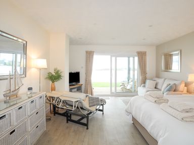 A bedroom with a bed with towels a sofa a lounge chair a dresser with a model sailboat a lamp and sliding glass doors at White Sails in Y Felinheli