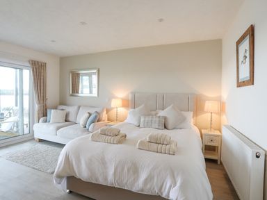 A bedroom with a bed sofa two bedside tables with lamps a mirror and a sliding glass door at White Sails in Y Felinheli