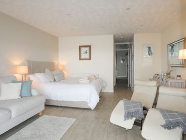 A bedroom with a bed sofa two chairs a dresser and framed bird pictures at White Sails in Y Felinheli