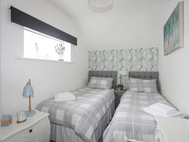 A bedroom with two single beds a bedside table with a lamp and decorative items at White Sails in Y Felinheli