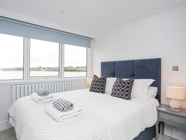 A bedroom with a bed with patterned pillows and folded towels by a large window at White Sails in Y Felinheli
