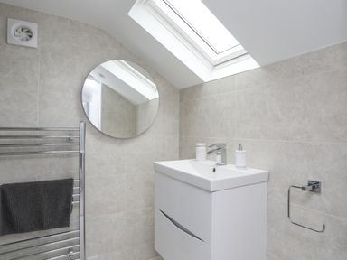 A bathroom with a white sink unit round mirror skylight and a towel on a metal rail at White Sails in Y Felinheli