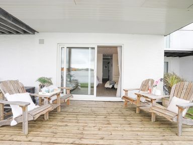 A covered patio with wooden chairs and small tables outside sliding glass doors at White Sails in Y Felinheli