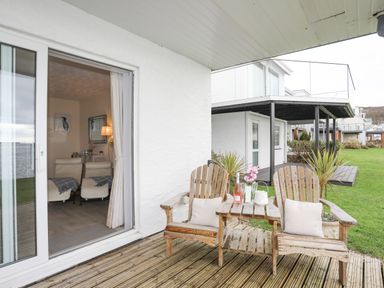 A patio with wooden chairs and table with bottle and flowers next to a glass sliding door showing a living room at White Sails in Y Felinheli