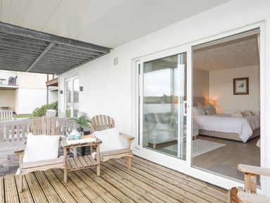 A patio with wooden chairs and a small table outside a bedroom with a bed and a framed picture at White Sails in Y Felinheli